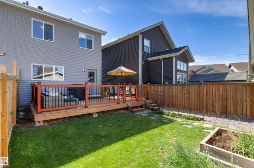 Expansive fenced backyard featuring a wooden deck with dark orange railings, a grassy lawn, and a raised garden bed - 4306 Prowse Link Link Sw, Edmonton, AB 
