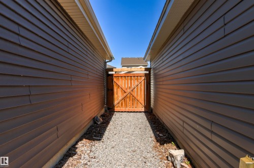 Side yard access featuring a wood gate, gravel pathway, and horizontal siding - 4306 Prowse Link Link Sw, Edmonton, AB 