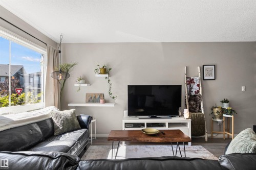Large window with white trim, suspended light fixture, wall-mounted shelving, wood-finish flooring, and light-toned walls - 4306 Prowse Link Link Sw, Edmonton, AB 
