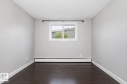 Dark wood-finish flooring with white trim, light gray walls, and a white-framed window - 