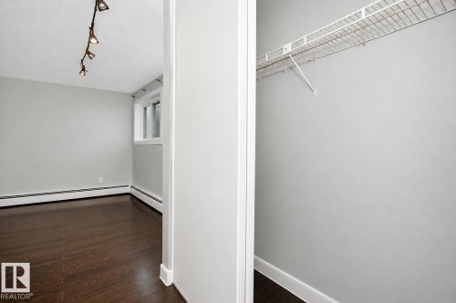Wood-finish flooring, track lighting, and a window with white trim, complemented by a closet featuring wire shelving - #203 2624 Mill Woods Rd E Nw, Edmonton, AB 