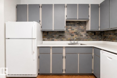 Kitchen featuring gray cabinetry, white countertops, stainless steel sink, and brick-style backsplash - #203 2624 Mill Woods Rd E Nw, Edmonton, AB 