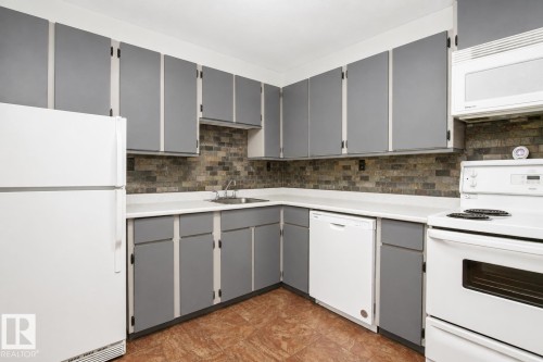 Kitchen featuring gray cabinetry, white countertops, tile backsplash, stainless steel sink, and integrated appliances - #203 2624 Mill Woods Rd E Nw, Edmonton, AB 