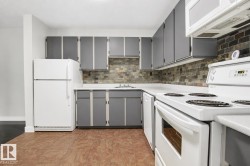 Kitchen featuring L-shaped counter space, gray cabinetry, white appliances, and a tiled backsplash - 