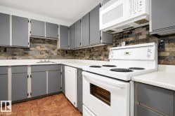 Kitchen featuring gray cabinetry, light-toned countertops, a multi-tone tile backsplash, and a white oven/stove combination - 