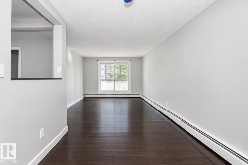 Dark wood-finish flooring, light grey painted walls, and a large window with white trim - #203 2624 Mill Woods Rd E Nw, Edmonton, AB 