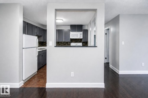 Kitchen pass-through with a dark countertop and white cabinetry - #203 2624 Mill Woods Rd E Nw, Edmonton, AB 