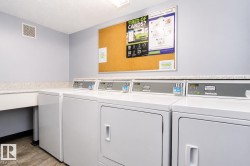 Community laundry facility featuring multiple commercial-grade washers and dryers, a built-in counter space, sink, and light-toned walls - 