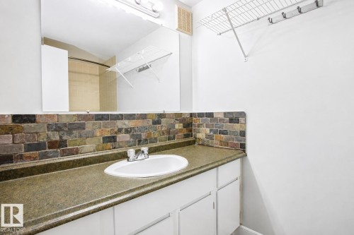 Vanity with integrated sink, stone-look countertop, and brick-patterned backsplash - #203 2624 Mill Woods Rd E Nw, Edmonton, AB 