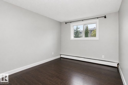 Dark wood-finish flooring with white trim, light gray walls, and a window with white casing - #203 2624 Mill Woods Rd E Nw, Edmonton, AB 