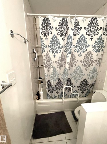 White ceramic tile flooring, white subway tile shower surround, and a white bathtub with a built-in grab bar - #D1 1 Garden Grove Nw, Edmonton, AB 