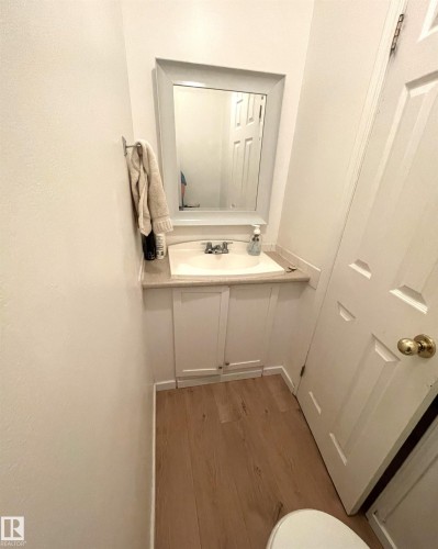 Powder room featuring a framed mirror, a vanity with a drop-in sink, white cabinetry, and wood-finish flooring - #D1 1 Garden Grove Nw, Edmonton, AB 