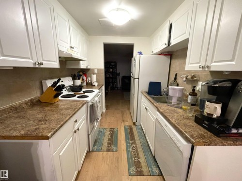 Galley kitchen featuring white cabinetry, light wood-finish flooring, and a stone-look countertop - #D1 1 Garden Grove Nw, Edmonton, AB 