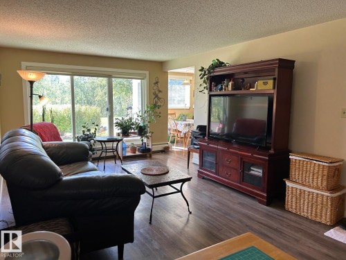 Wide sliding glass door with exterior foliage, wood-finish flooring, and light-toned wall finishes - #112 4404 122 St Nw, Edmonton, AB 