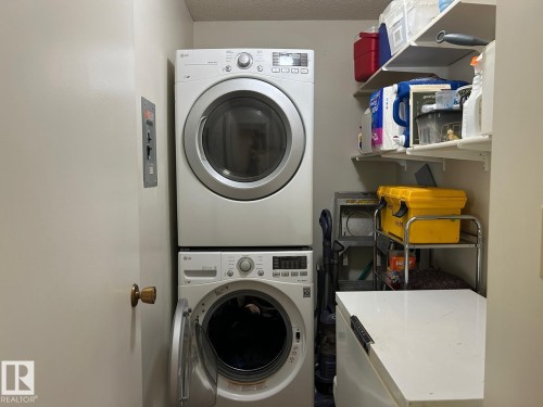 Laundry area with a stacked washer and dryer, fixed wall shelving, and a built-in counter surface - #112 4404 122 St Nw, Edmonton, AB 