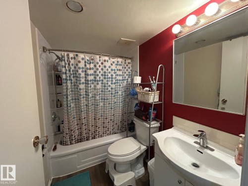White tub and shower combination with built-in shelving, wood-finish flooring, vanity with integrated sink, and white tile backsplash - #112 4404 122 St Nw, Edmonton, AB 