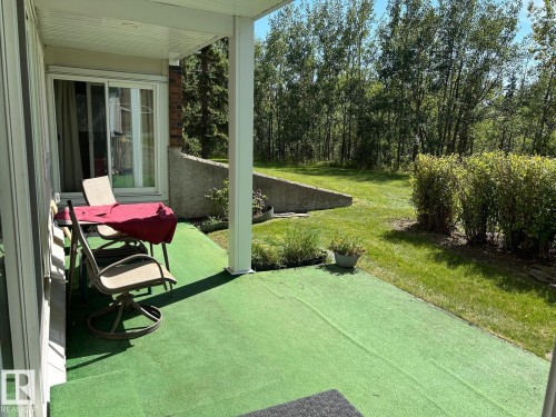 Covered patio area with a sliding glass door, a retaining wall, and verdant landscaping - #112 4404 122 St Nw, Edmonton, AB 
