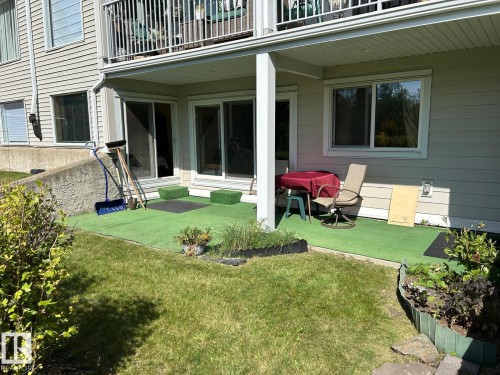 Ground-level patio with artificial turf, bordered by a manicured lawn - #112 4404 122 St Nw, Edmonton, AB 