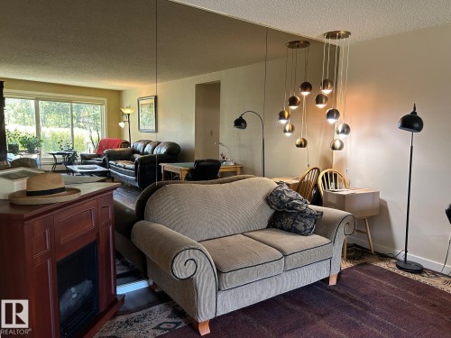 Wall-mounted mirror paneling, a multi-pendant ceiling light fixture, wood-finish flooring, and a large window with outdoor scenery - #112 4404 122 St Nw, Edmonton, AB 