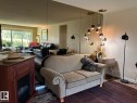 Wall-mounted mirror paneling, a multi-pendant ceiling light fixture, wood-finish flooring, and a large window with outdoor scenery - #112 4404 122 St Nw, Edmonton, AB 
