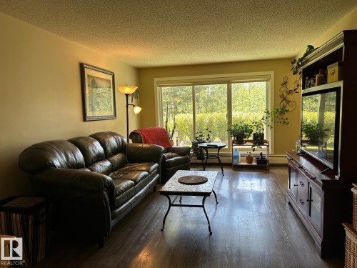 Wood-finish flooring throughout, complemented by a wide window opening to exterior foliage - #112 4404 122 St Nw, Edmonton, AB 
