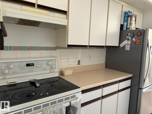 White cabinetry with wood-finish trim, ceramic tile backsplash, smooth-top electric range, and laminate countertops - #112 4404 122 St Nw, Edmonton, AB 