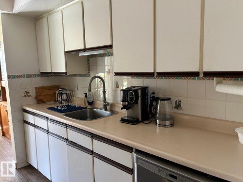 White upper and lower cabinetry, stainless steel sink with a gooseneck faucet, light-toned countertop, and tiled backsplash - #112 4404 122 St Nw, Edmonton, AB 