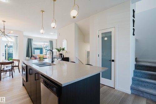 Kitchen island with a light-toned countertop, integrated sink, and modern pendant lighting - 7017 52 Avenue, Beaumont, AB 