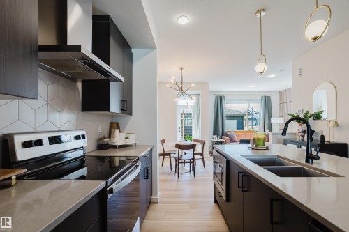 Kitchen featuring stainless steel appliances, dark wood-finish cabinetry, light stone-finish countertops, and a geometric tile backsplash - 7017 52 Avenue, Beaumont, AB 