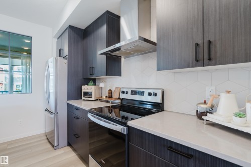 Kitchen featuring wood-finish cabinetry, stainless steel appliances, light countertops, and a geometric tile backsplash - 7017 52 Avenue, Beaumont, AB 