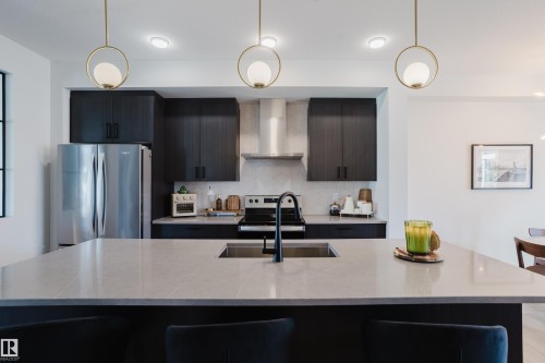 Kitchen featuring a large island with an undermount sink, dark wood-finish cabinetry, stainless steel appliances, and pendant lighting - 7017 52 Avenue, Beaumont, AB 