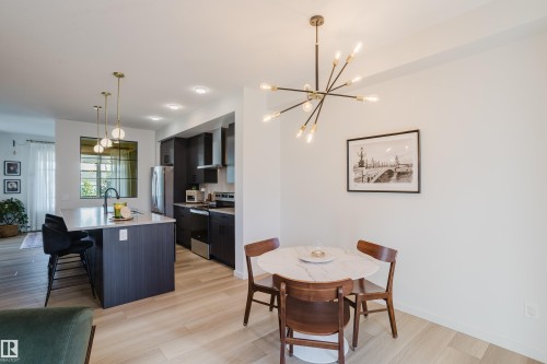 Open-concept living space featuring wood-finish flooring, a contemporary dining light fixture, and a kitchen with dark cabinetry, stainless steel appliances, and an island with pendant lighting - 7017 52 Avenue, Beaumont, AB 