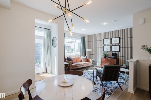 Open-concept living space featuring a modern sputnik chandelier, wood-finish flooring, a decorative slat wall, and recessed lighting - 7017 52 Avenue, Beaumont, AB 
