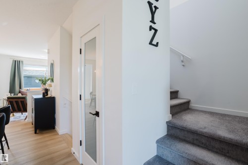 Light wood-finish flooring, white walls, and a staircase featuring gray carpeting and a white handrail - 7017 52 Avenue, Beaumont, AB 