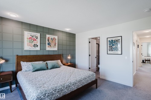 Accent wall with geometric patterning, recessed ceiling lighting, wood-frame bed, and a doorway to an adjoining bathroom - 7017 52 Avenue, Beaumont, AB 
