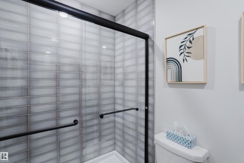 Glass-enclosed shower with black-framed sliding door, light-toned horizontal tile, and black grab bars - 7017 52 Avenue, Beaumont, AB 