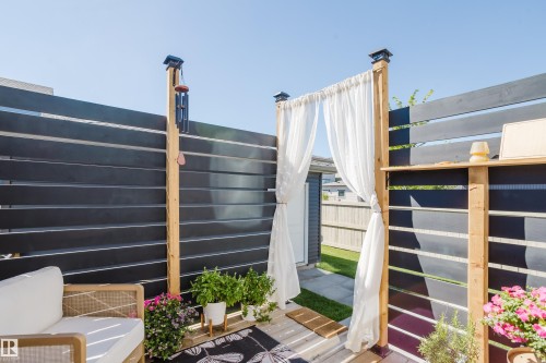 Dark horizontal slat fencing with natural wood posts, white sheer curtains, and a built-in outdoor shelf - 7017 52 Avenue, Beaumont, AB 