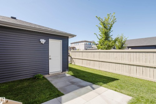 Exterior featuring horizontal siding, a white service door, concrete pavers, and a wood privacy fence - 7017 52 Avenue, Beaumont, AB 