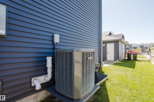 Blue horizontal siding, central air conditioning unit, manicured lawn, white back door, and fencing - 7017 52 Avenue, Beaumont, AB 