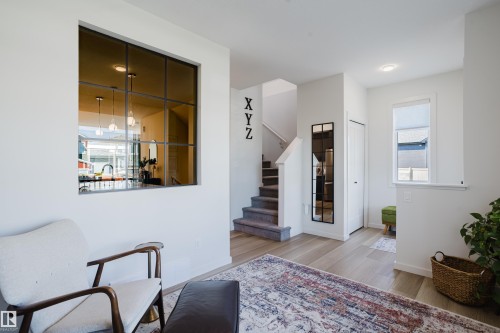 Wood-finish flooring, a contemporary staircase with carpeted treads, and a built-in window overlooking a kitchen space - 7017 52 Avenue, Beaumont, AB 