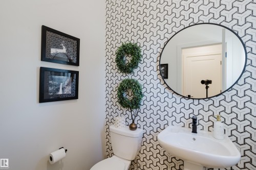 Geometric patterned accent wall, pedestal sink, matte black faucet, and a round wall mirror - 7017 52 Avenue, Beaumont, AB 