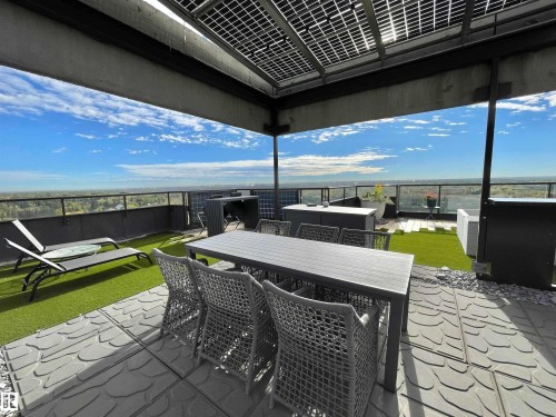 Rooftop terrace with a glass perimeter railing, patterned patio pavers, and artificial turf sections - #904 8220 Jasper Av Nw, Edmonton, AB 