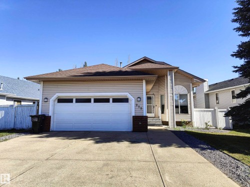 Front exterior featuring a concrete driveway, attached garage with panel doors, and a partial white privacy fence - 215 Peter Close Nw, Edmonton, AB 
