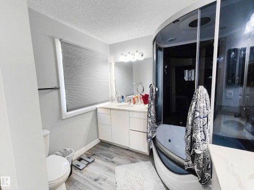 Curved glass shower enclosure with integrated tub, single vanity with light-toned cabinetry, light-toned countertop, and wood-finish flooring - 215 Peter Close Nw, Edmonton, AB 