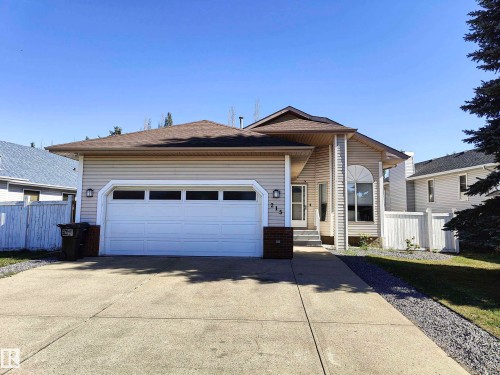Beige siding exterior with an attached garage, concrete driveway, arched window, and white fencing - 215 Peter Close Nw, Edmonton, AB 