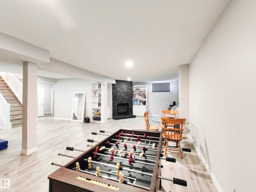 Expansive open-concept room featuring wood-finish flooring, a built-in fireplace with a dark stone surround, and recessed lighting - 215 Peter Close Nw, Edmonton, AB 
