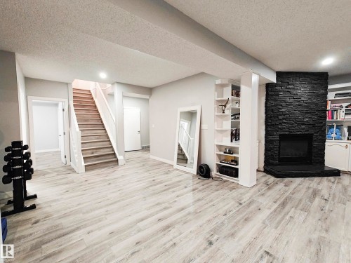 Spacious lower level featuring wood-finish flooring, a stone-clad fireplace, integrated shelving, and a prominent staircase with white banisters - 215 Peter Close Nw, Edmonton, AB 