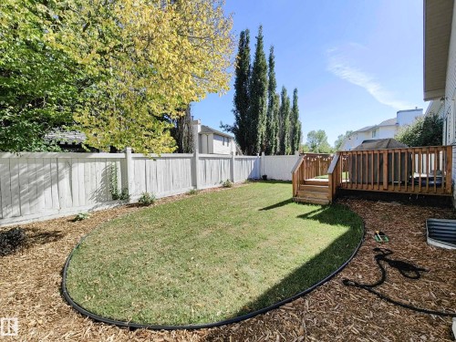 Expansive backyard featuring a manicured lawn, wood-toned deck, perimeter fencing, and mature trees - 215 Peter Close Nw, Edmonton, AB 
