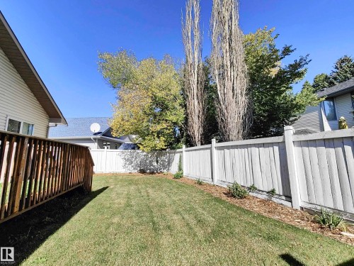 Fenced backyard featuring a wood deck, manicured lawn, and mature trees - 215 Peter Close Nw, Edmonton, AB 