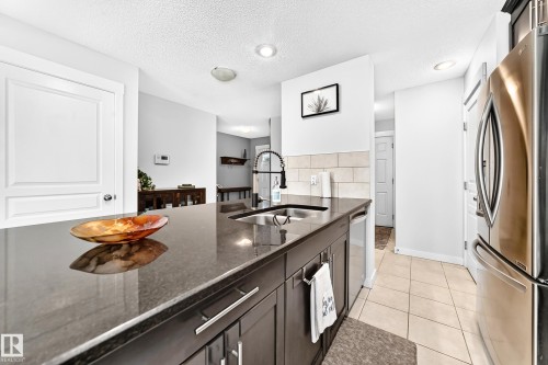 Kitchen island with dark countertop, stainless steel sink with a gooseneck faucet, integrated dishwasher, and recessed lighting - 16832 53 Street Nw, Edmonton, AB 